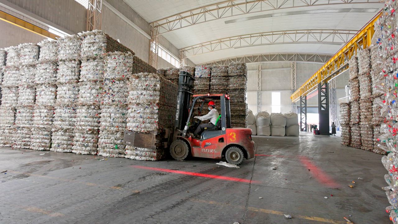 After crushing the PET bottles, a forklift operator moving stacked crushed PET bottles 

This shows...